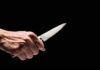 Hand holding a knife against a black background.