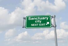 Green road sign saying sanctuary city next exit