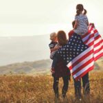 Mastering In-Law Dynamics: Key Strategies for Empathy and Connection Family in field with American flag, children on shoulders.