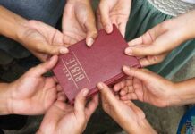 Multiple hands holding a red Bible together.