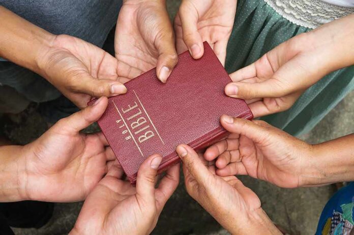 133452947 featured image Multiple hands holding a red Bible together.