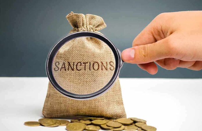 1341325112 featured image Hand holding magnifying glass over sack labeled "Sanctions".