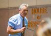 Man speaking with microphone outside building with lettering