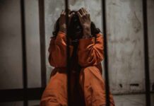 Person in orange jumpsuit sitting in a cell