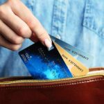 Discover Luxury Travel Cards to Stretch Your Summer Budget Further Hand holding credit cards over a brown purse.