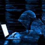 Are your forgotten social media profiles putting you at risk? Hooded figure using laptop with code background.