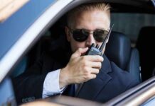 Man in suit using walkie-talkie in car.