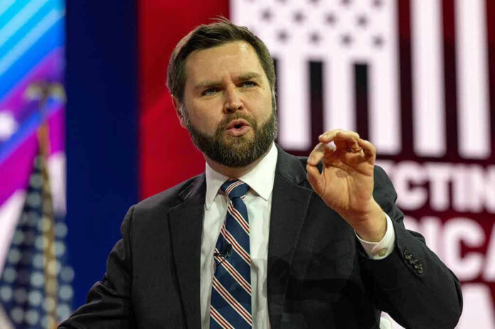 Man in suit speaking at event, background with flag