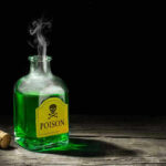 Green poison bottle with cork on wooden surface.