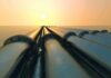 Industrial pipes extending towards the horizon over water during sunset