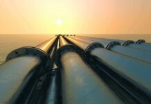 Industrial pipes extending towards the horizon over water during sunset