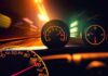 Close up of a car dashboard with speedometer and tachometer illuminated at night