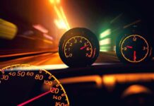 Close up of a car dashboard with speedometer and tachometer illuminated at night