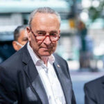 Man in suit and red glasses standing outside.