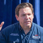 Man speaking, wearing a blue Desantis for President shirt.