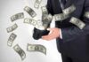 A businessman holding a wallet with money flying out