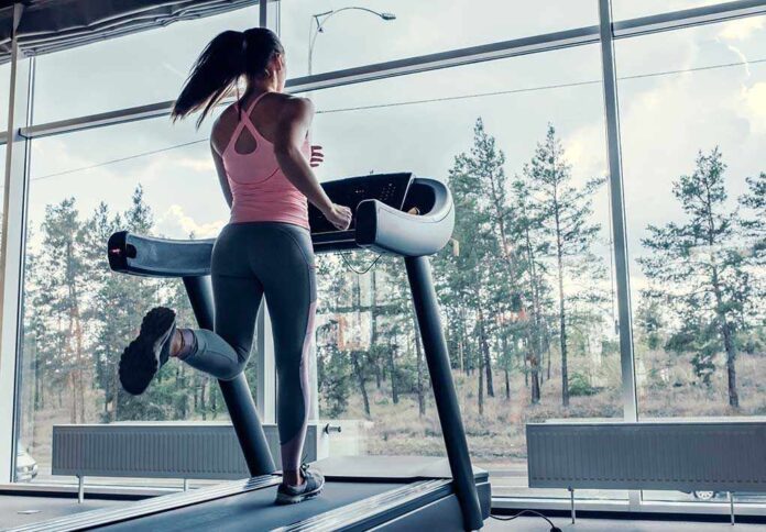 A woman running on a treadmill in a gym with large windows