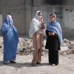 Three women in traditional attire standing in an urban setting with debris in the background