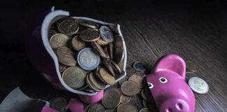 A broken pink piggy bank with coins spilling out onto a wooden surface