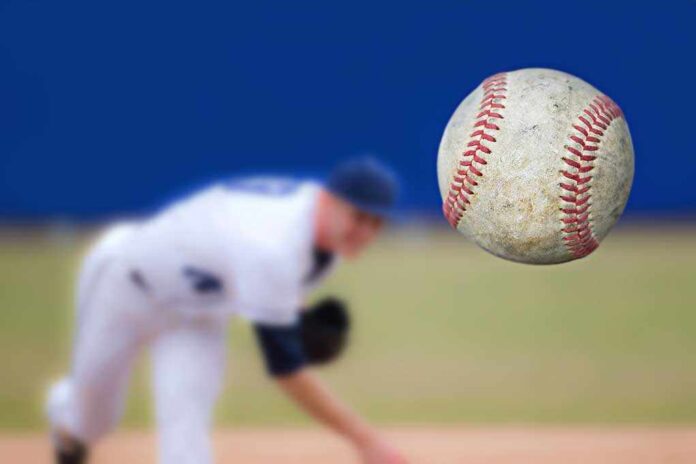 A baseball in mid air with a pitcher in the background preparing to throw