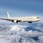 A white airplane flying above fluffy clouds in a blue sky