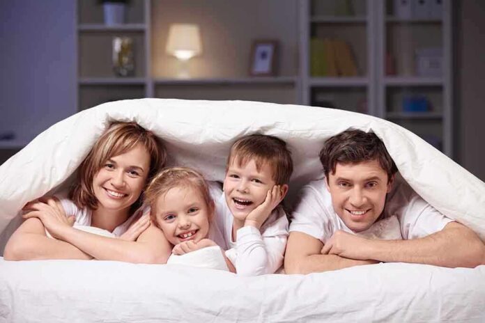 A family of four smiling and cuddling under a blanket