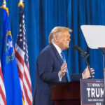 Person speaking at podium with flags in background