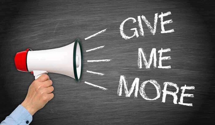 A hand holding a megaphone with the words GIVE ME MORE on a blackboard background