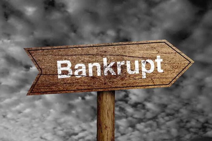 Wooden arrow sign pointing towards the word Bankrupt against a cloudy background