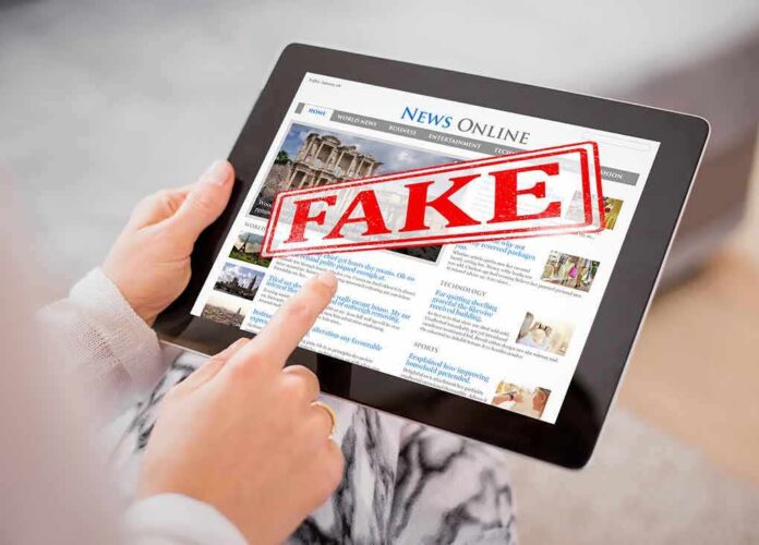 Person holding a tablet displaying a news website with a FAKE stamp