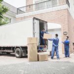 Workers unloading boxes from a moving truck in a residential driveway