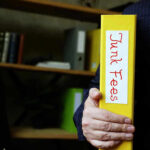 Hand holding folder labeled Junk Fees bookshelf background
