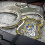 ICE Grabs Illegal Police Recruit Mid-Training Handcuffs, officer badge, and firearm on textured surface.