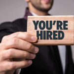 Person holding a Youre Hired sign.