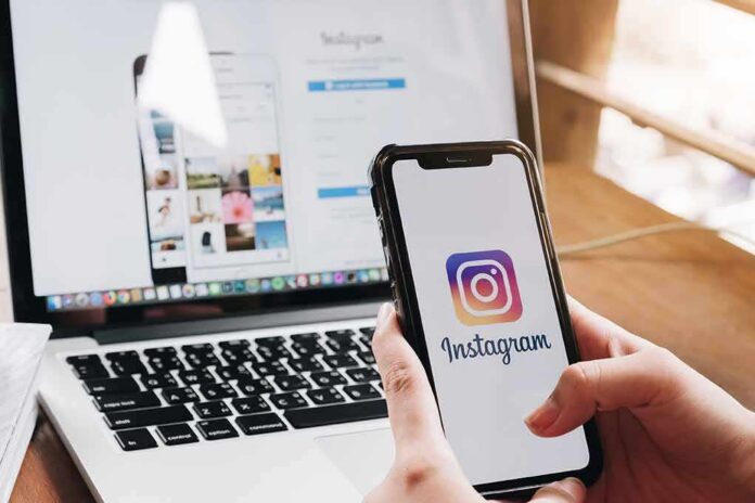 Person holding a smartphone displaying the Instagram logo with a laptop in the background