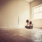 A child sitting alone in an empty room, covering their face with their hands