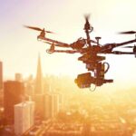 A drone flying over a city skyline during sunset