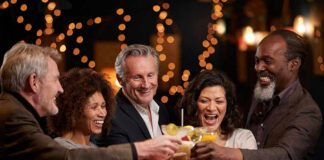 People laughing while clinking glasses at a bar