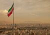 Iranian flag waving over a city skyline with mountains in the background