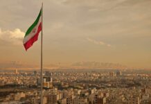 Iranian flag waving over a city skyline with mountains in the background