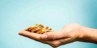 A hand holding a stack of gold coins against a light blue background