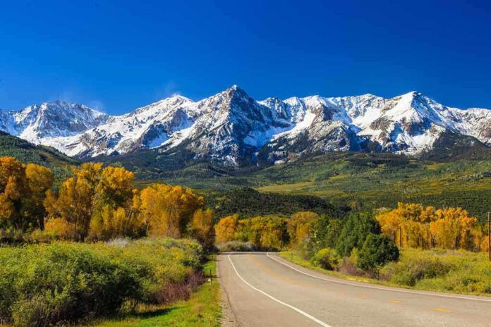 Scenic view of snow-capped mountains with autumn trees and a winding road