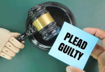 A wooden gavel next to a hand holding a blue card that says 'PLEAD GUILTY'