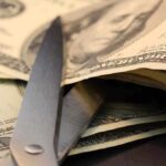 Scissors cutting through a stack of dollar bills