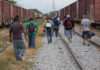 People walking along train tracks carrying backpacks