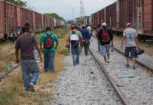 People walking along train tracks carrying backpacks