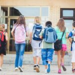 AI Takeover: Teachers in Control? Group of children walking towards a school entrance with backpacks