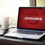 Laptop screen displaying CENSORED beside coffee and phone