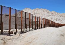 3,000-Foot Cartel Tunnel Under U.S. Port A long border wall stretches across a desert landscape with mountains in the background