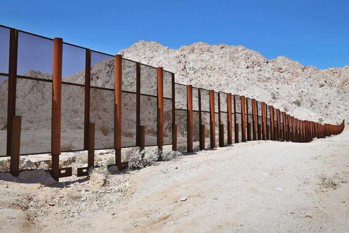 Large,Steel,Fence,Protecting,The,Border,Between,Mexico,And,The A long border wall stretches across a desert landscape with mountains in the background